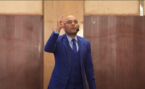 Harshvardhan Jain wearing a blue suit explaining the difference between books and TV